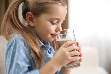 Photo of Cute little child drinking tasty chocolate milk indoors, closeup. Space for text