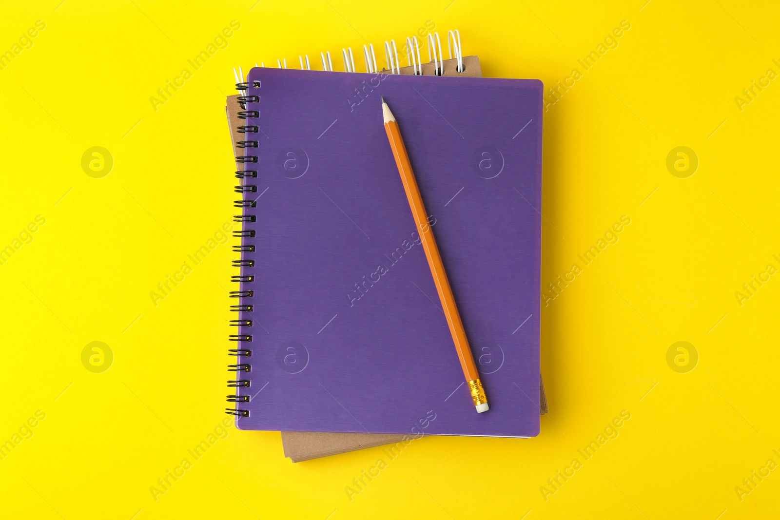 Photo of Notebooks with pencil on yellow background, top view