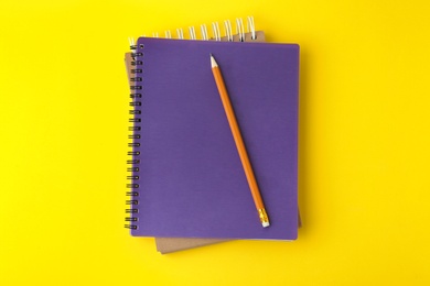 Photo of Notebooks with pencil on yellow background, top view