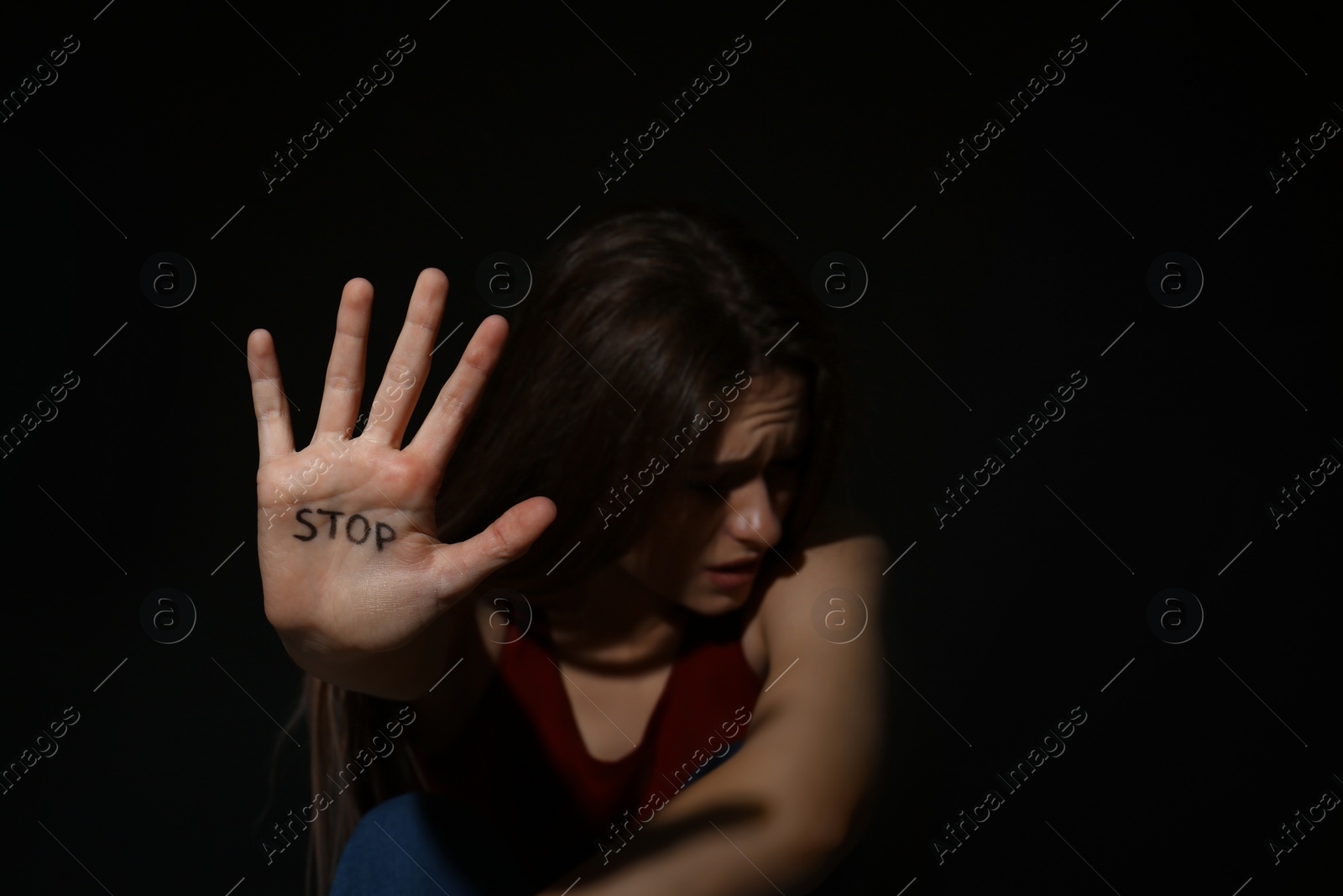 Photo of Abused young woman showing palm with word STOP against black background, focus on hand. Domestic violence concept