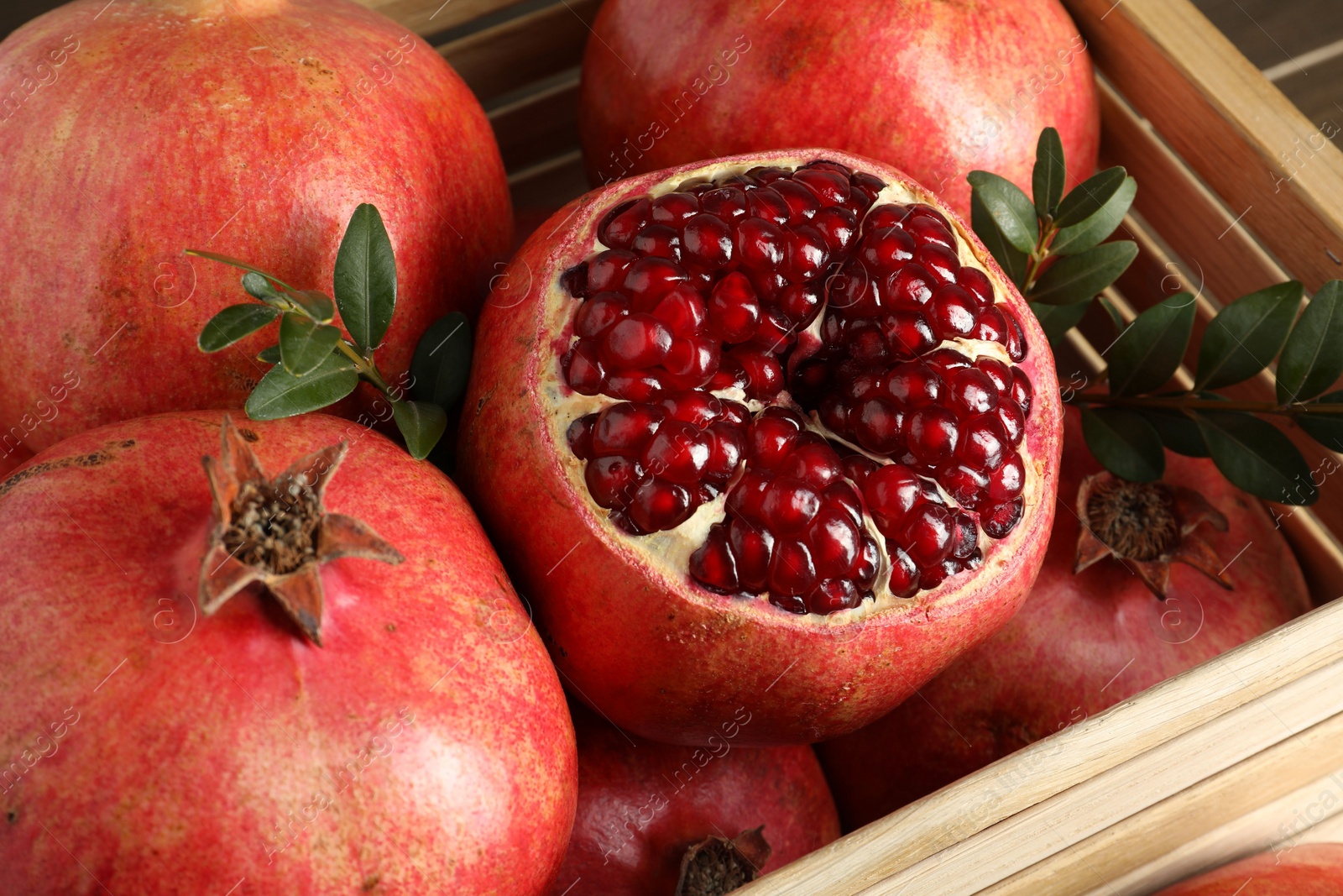 Photo of Fresh ripe pomegranates in wooden crate, closeup