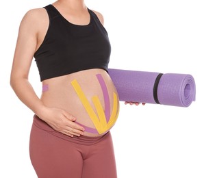 Sporty pregnant woman with kinesio tapes holding yoga mat on white background, closeup