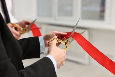 Photo of People cutting red ribbon with scissors indoors, closeup