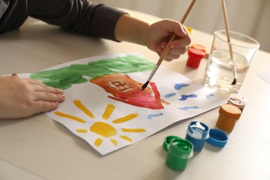 Photo of Little boy drawing picture with brush at wooden table indoors, closeup. Child`s art