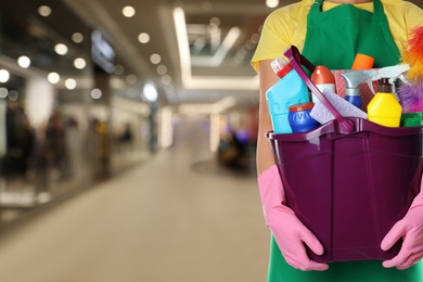 Image of Woman holding bucket with cleaning supplies in shopping mall, closeup. Space for text
