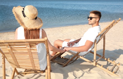 Photo of Young couple relaxing in deck chairs on beach