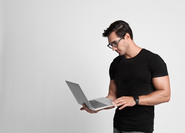 Handsome young man with laptop on grey background. Space for text