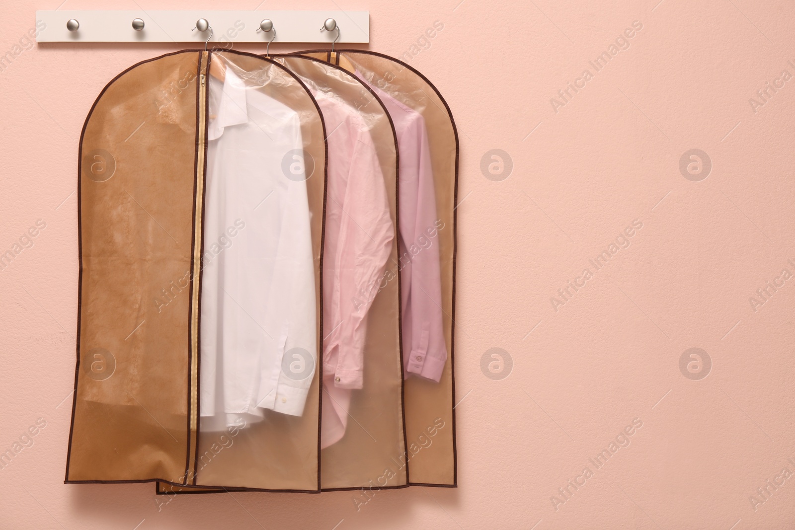 Photo of Garment bags with clothes hanging on light wall. Space for text