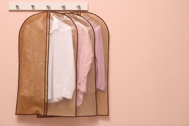 Photo of Garment bags with clothes hanging on light wall. Space for text