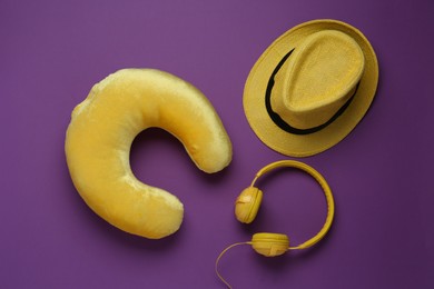 Photo of Yellow travel pillow, hat and headphones on purple background, flat lay