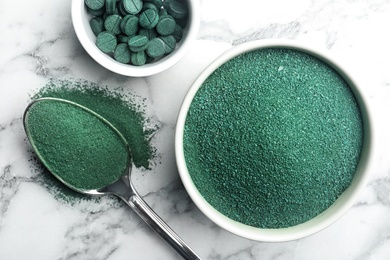 Photo of Composition with spirulina algae powder and pills on marble background, top view