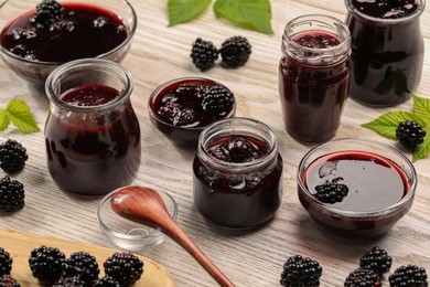 Photo of Tasty blackberry jam and fresh berries on white wooden table