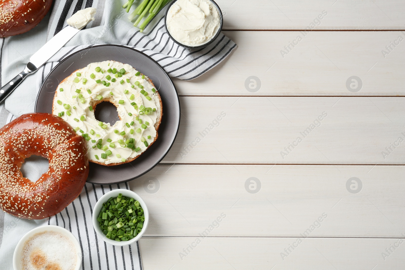 Photo of Delicious bagel with cream cheese and green onion on white wooden table, flat lay. Space for text