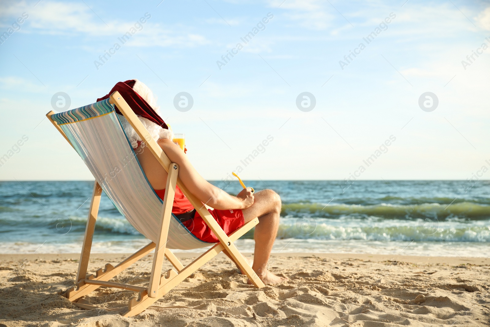 Photo of Santa Claus relaxing in chair on beach, space for text. Christmas vacation