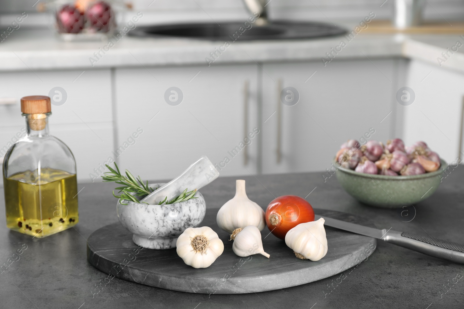 Photo of Fresh raw garlic, onion, rosemary and oil on grey table