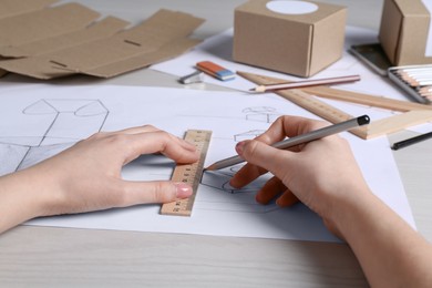 Woman creating packaging design at light wooden table, closeup