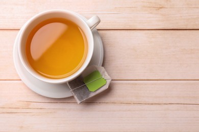 Photo of Tea bag and cup of hot beverage on light wooden table, top view. Space for text