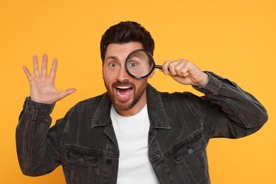 Photo of Emotional man looking through magnifier glass on yellow background