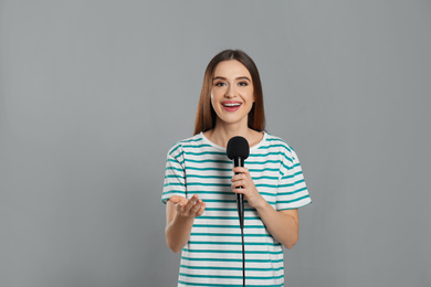 Photo of Young female journalist with microphone on grey background