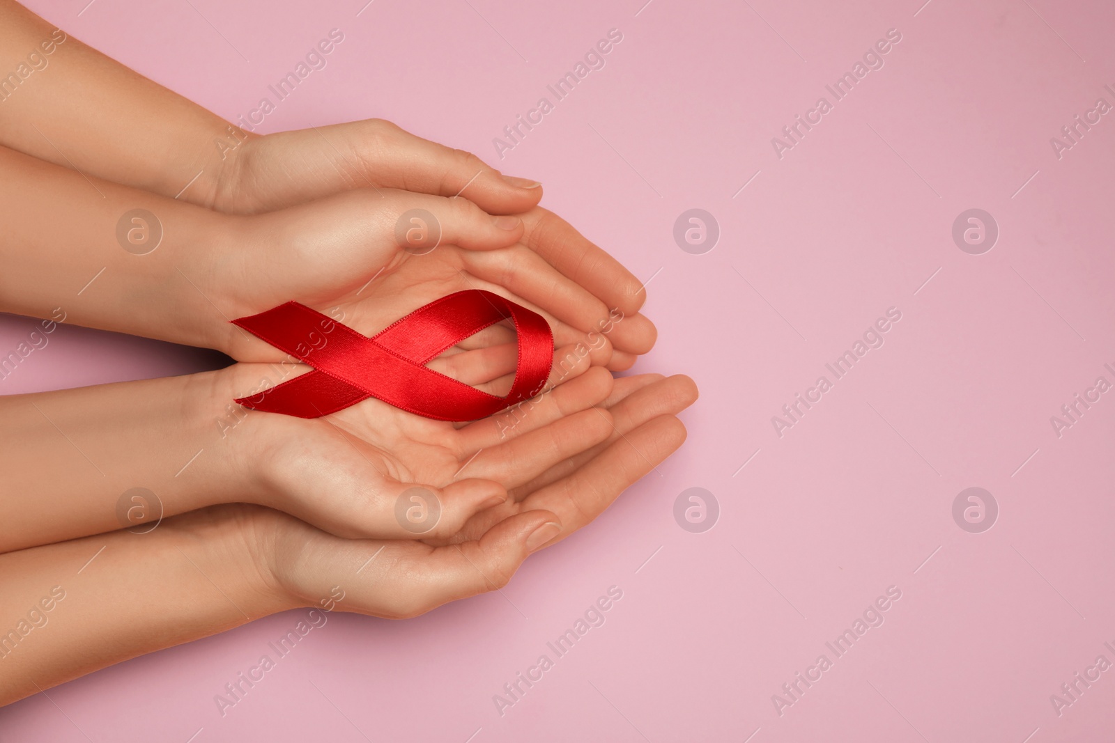 Photo of Woman and girl holding red ribbon on pink background, top view with space for text. AIDS disease awareness