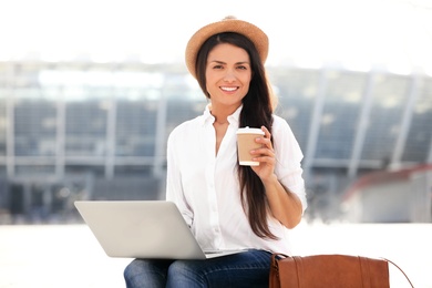 Photo of Beautiful woman with cup of coffee using laptop outdoors on sunny day