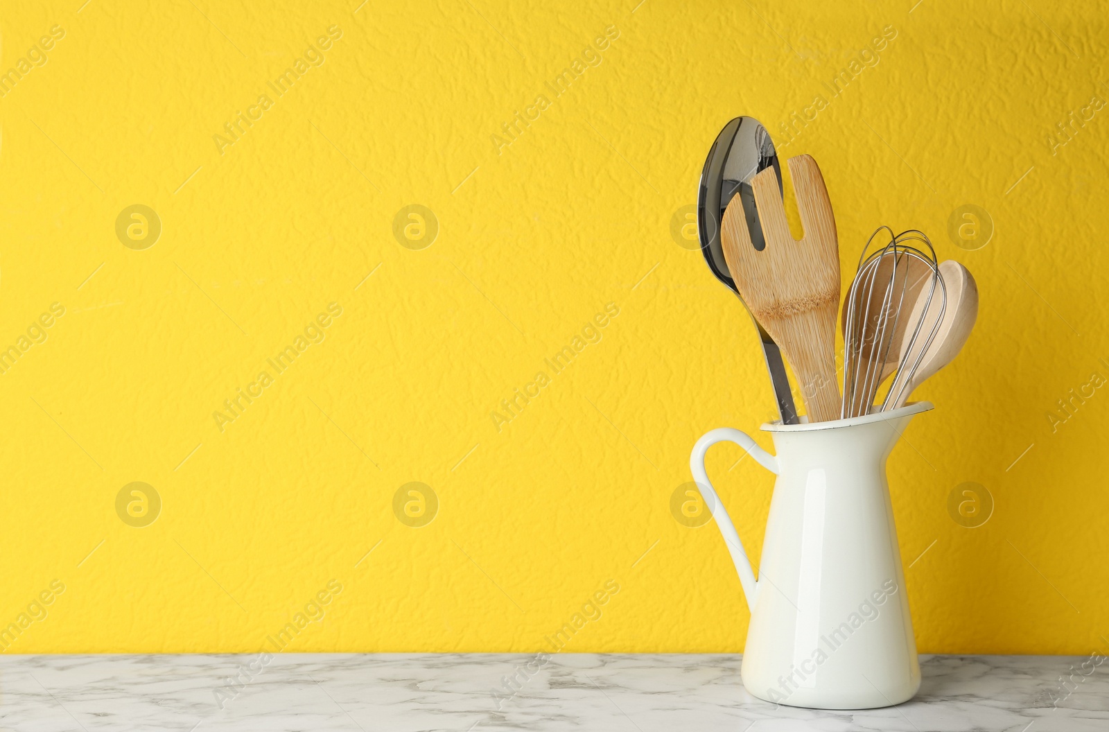 Photo of Jug with kitchen utensils on marble table against yellow background. Space for text