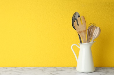 Jug with kitchen utensils on marble table against yellow background. Space for text