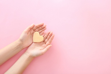 Woman holding wooden heart on color background, top view