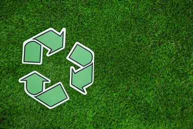 Paper recycling symbol on green grass, top view. Space for text