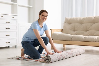 Smiling woman unrolling carpet with beautiful pattern on floor in room