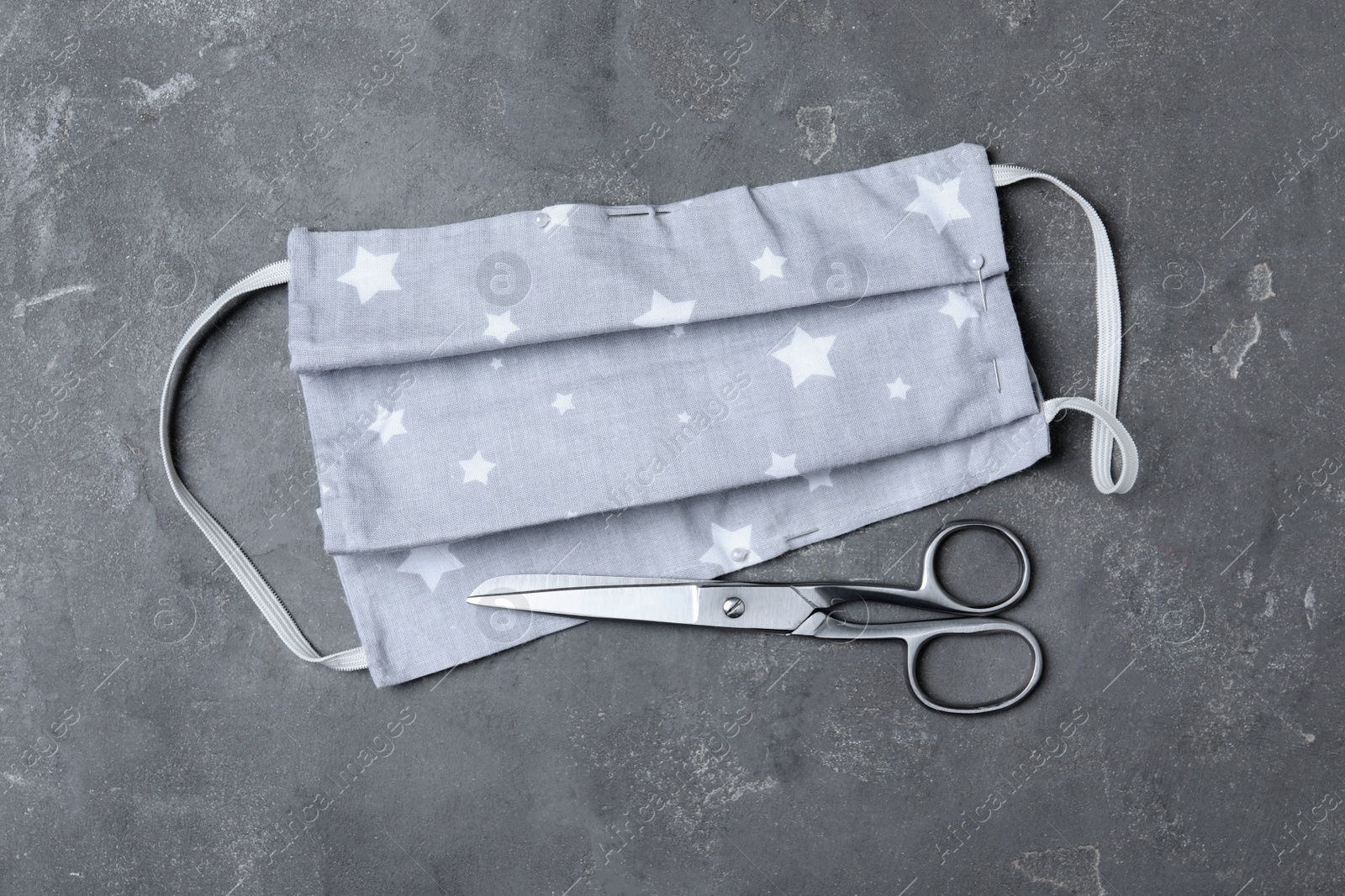 Photo of Homemade protective mask and scissors on grey stone background, flat lay. Sewing idea