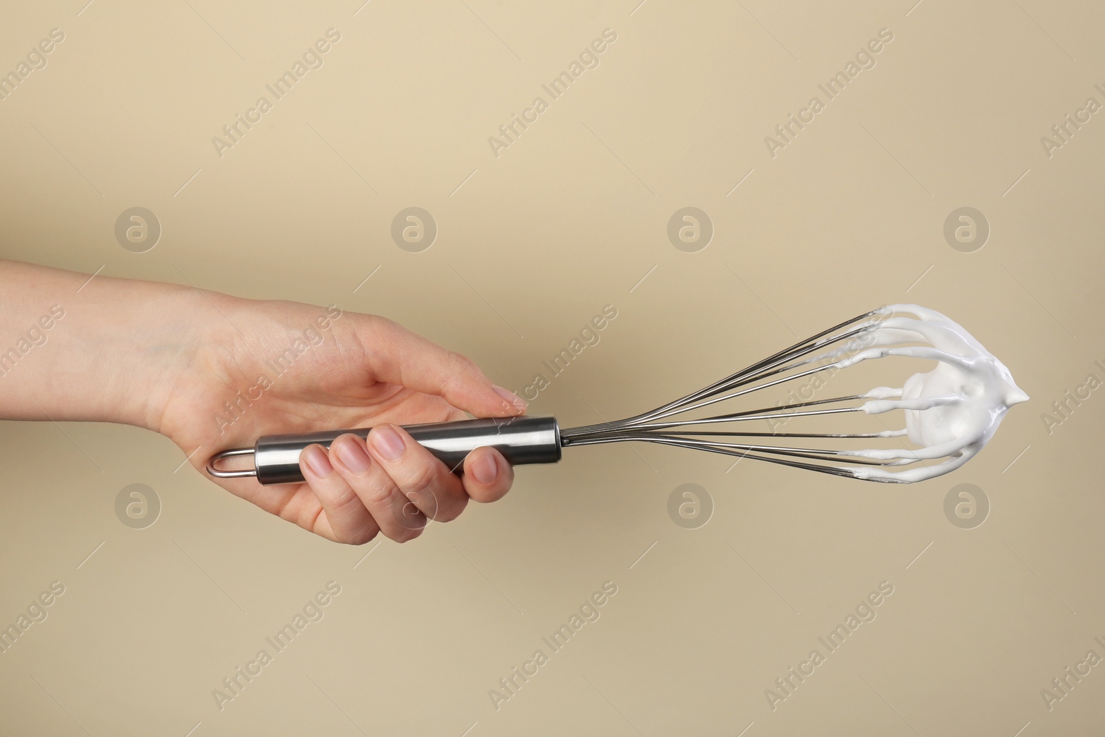 Photo of Woman holding whisk with whipped cream on beige background, closeup