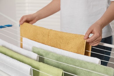 Photo of Woman hanging clean terry towels on drying rack indoors, closeup