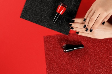 Woman with black manicure and nail polish bottles on color background, top view. Space for text