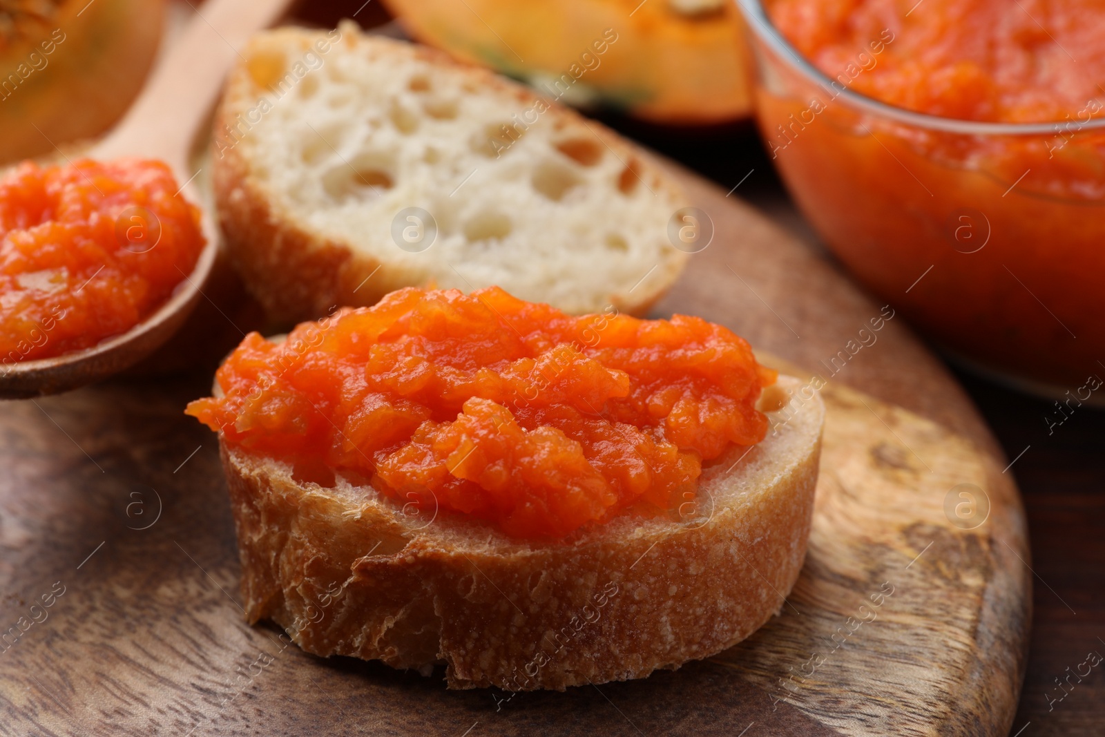 Photo of Slices of bread with delicious pumpkin jam and fresh pumpkin on wooden table, closeup