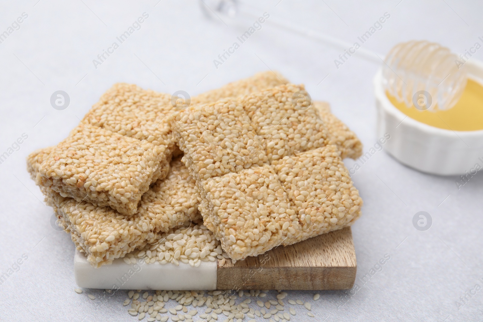 Photo of Delicious sesame kozinaki bars and honey on white table, closeup