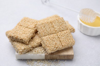 Photo of Delicious sesame kozinaki bars and honey on white table, closeup