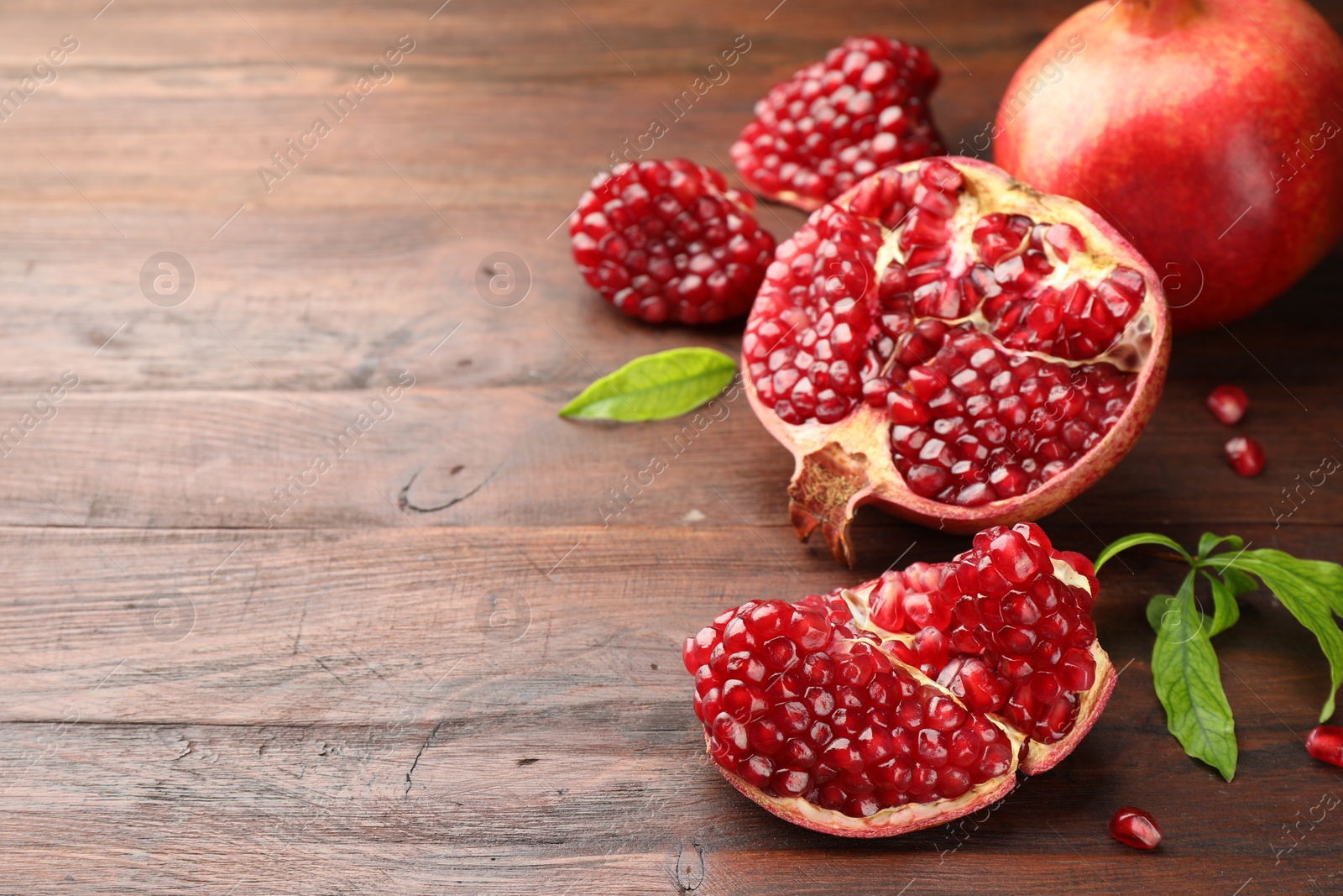 Photo of Fresh pomegranates and green leaves on wooden table, space for text