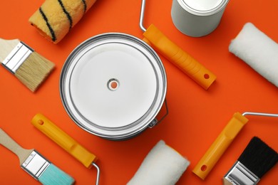 Cans of orange paint, brushes and rollers on color background, flat lay