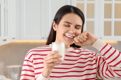 Happy woman with milk mustache holding glass of tasty dairy drink in kitchen