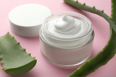 Jar with cream and cut aloe leaves on pink background, closeup