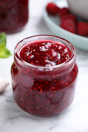 Photo of Delicious raspberry jam on white marble table, closeup