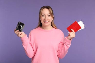 Happy young woman with passport, ticket and camera on purple background