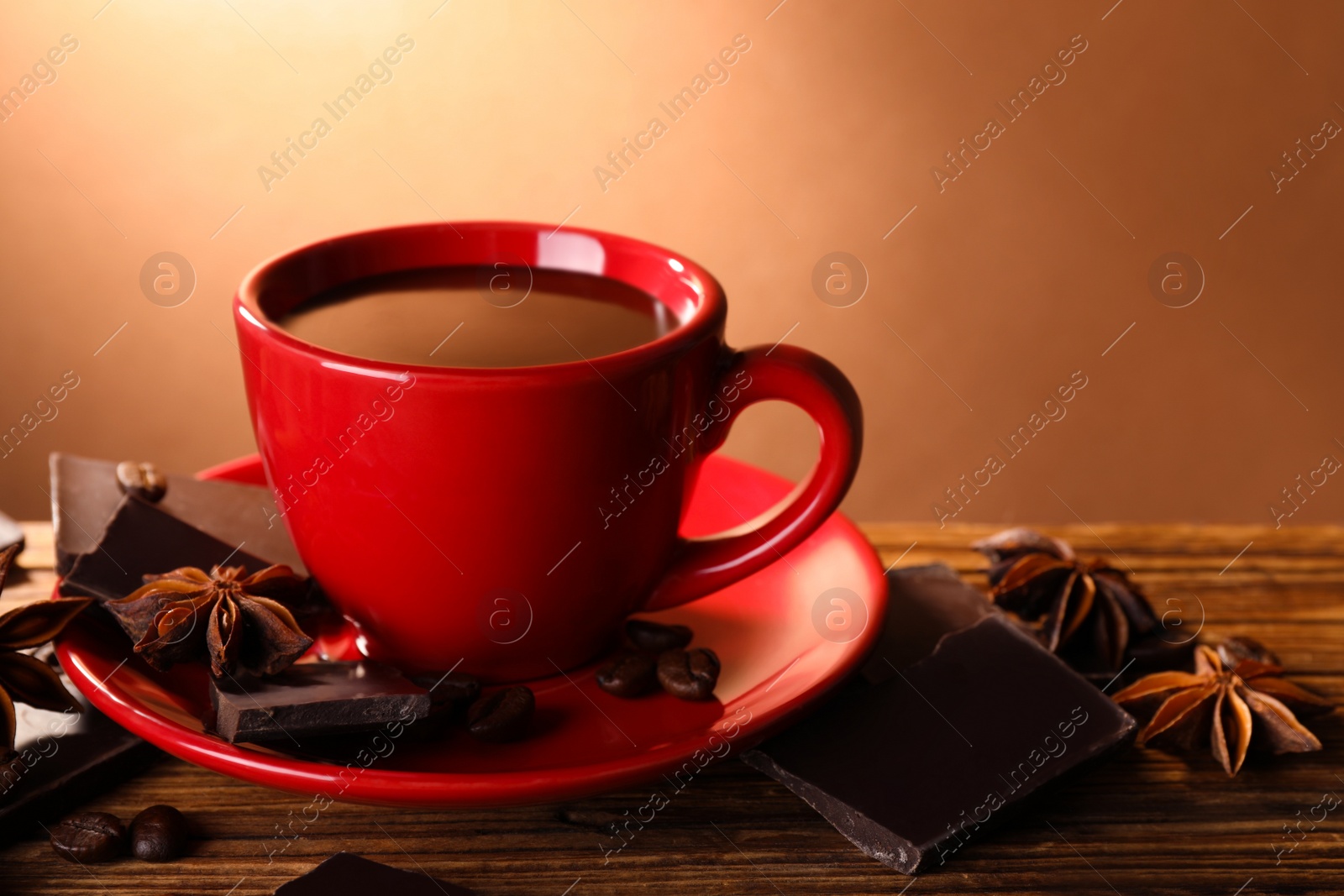 Photo of Cup of delicious hot chocolate, spices and coffee beans on wooden table. Space for text