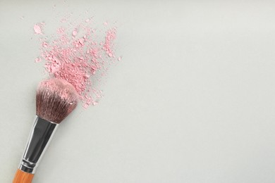 Photo of Makeup brush and scattered blush on light grey background, top view. Space for text