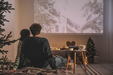 Photo of Couple watching Christmas movie via video projector at home, back view
