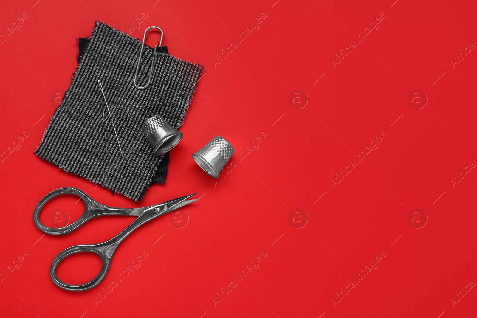 Photo of Thimbles and different sewing tools on red background, flat lay. Space for text