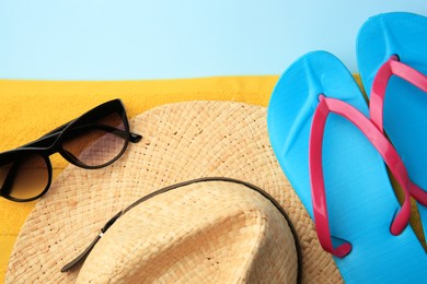 Photo of Flip flops, towel, sunglasses and hat on light blue background, flat lay. Beach accessories
