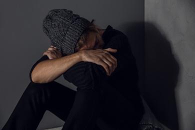 Stoned drug addict sitting near grey wall