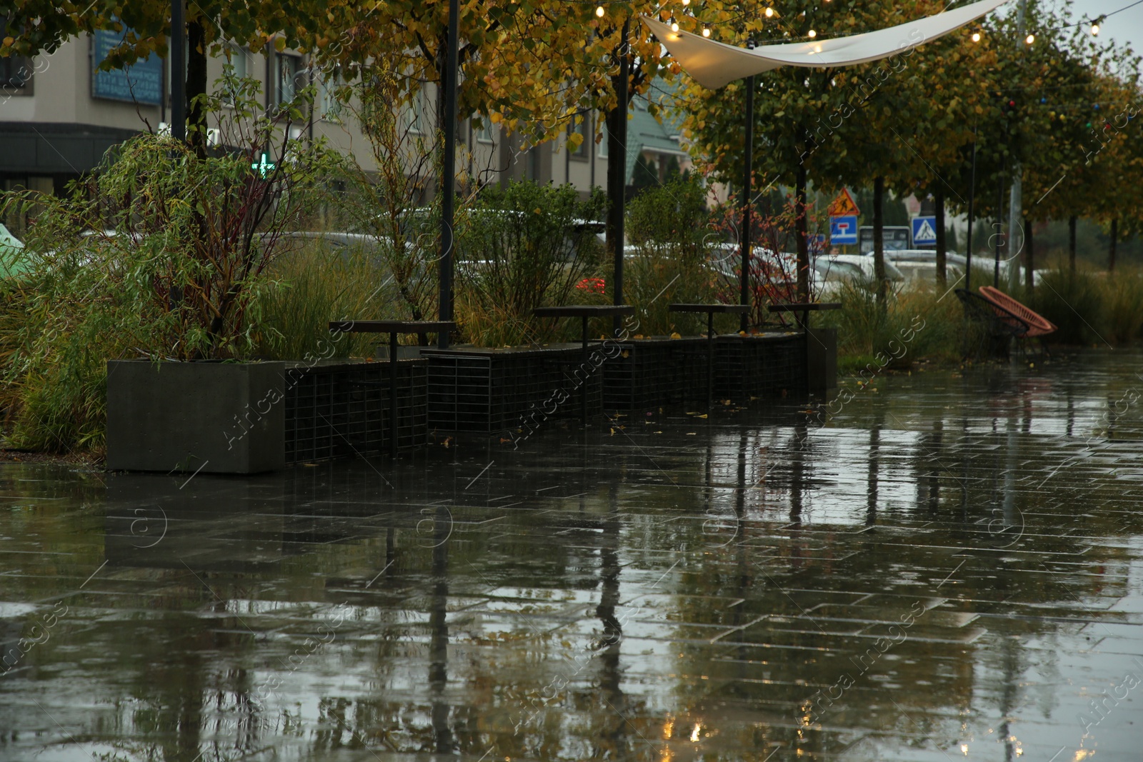 Photo of Wet outdoor cafe furniture and puddles on pavement after rain